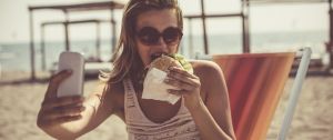 Une femme à la plage qui prend un selfie en mangeant un burger
