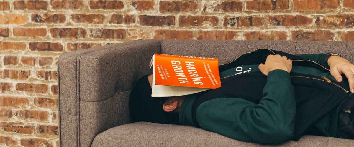 Les Français, rois de la procrastination ? Un homme qui dort sur un canapé avec un livre sur la tête