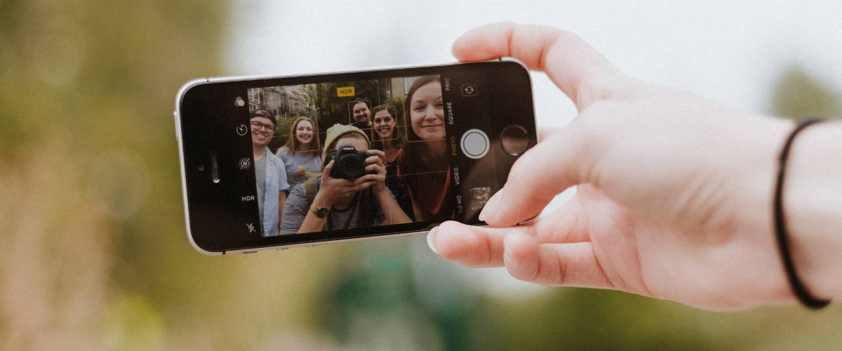 3 pistes pour une nouvelle influence Une main qui tient un smartphone en train de prendre un photo un groupe de personnes