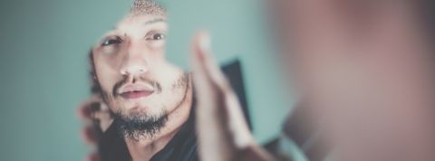 Un homme se regarde dans un miroir cassé