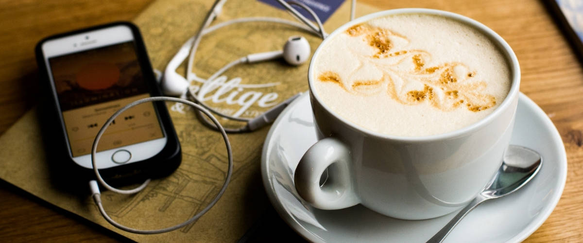 Luminary, le Netflix du podcast Tasse de cappuccino et smartphone avec des écouteurs sur une table.