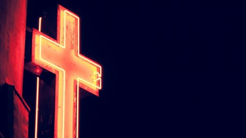 Néon en forme de croix chrétienne illuminé dans la nuit.