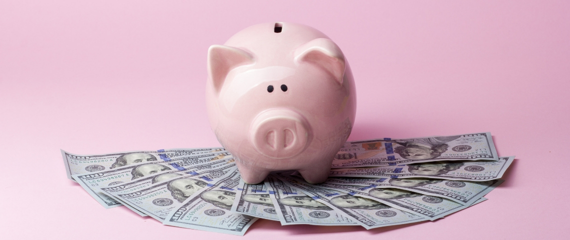 En France, les inégalités de salaire persistent Une tirelire cochon derrière une liasse de billets, sur un fond rose
