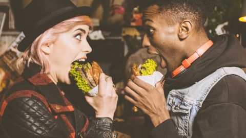 Une femme blanche et un homme noir qui mangent un burger en se regardant