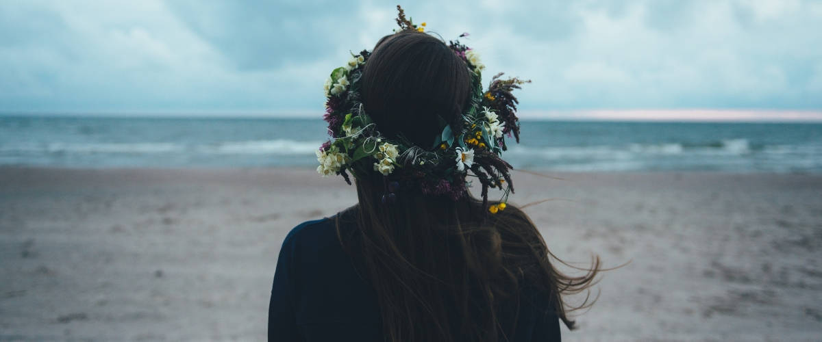 Les entreprises doivent-elles communiquer sur leurs actions RSE ? Une femme brune de dos face à la mer avec une couronne de fleurs dans les cheveux