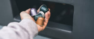 Un homme jette des capsules Nespresso dans une poubelle pour produits recyclables