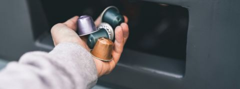 Un homme jette des capsules Nespresso dans une poubelle pour produits recyclables