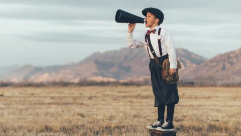 un petit garçon dans un champ sur un tabouret qui parle dans un haut parleur