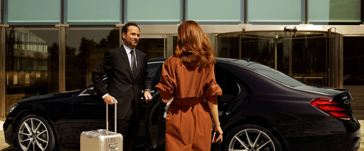 Le Uber de luxe arrive à Paris et il s'appelle Wheely Femme en robe vers une voiture berline accompagnée d'un chauffeurs tenant sa valise