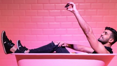 Un homme dans une baignoire rose, en train de prendre un selfie