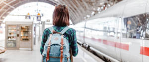 Une jeune fille de dos sur le quai d'une gare avec un sac à dos