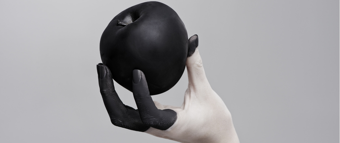 Entre gaspillage alimentaire et produits chimiques, tout le monde peut-il se passer du packaging ? Une main dont les doigts sont colorés en noir tenant une pomme peinte en noir