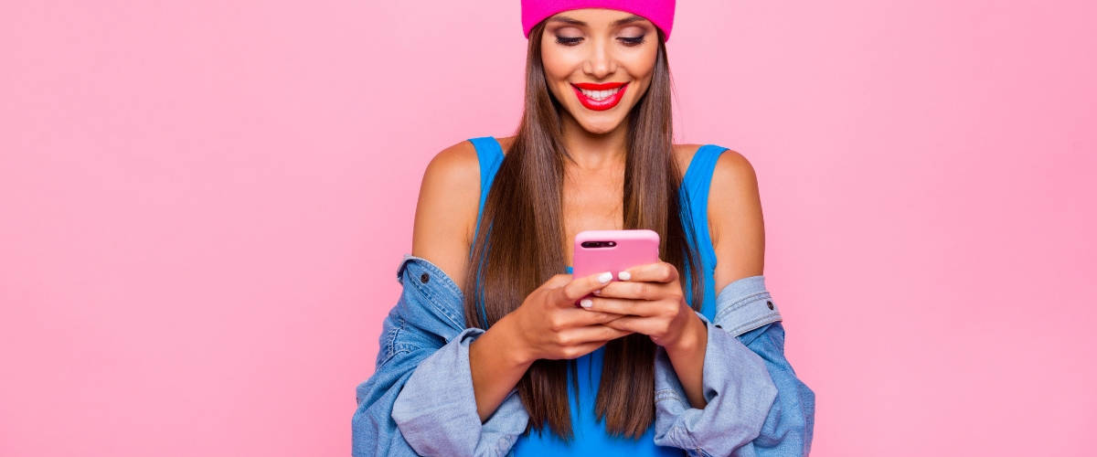 3 raisons de miser sur la messagerie instantanée Une femme en train d'écrire sur son smartphone devant un fond rose