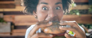 une jeune femme noire croque dans un burger vegan