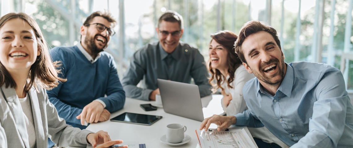 Quand les start-up se moquent enfin de leurs codes ridicules Groupe de salariés hilares autour d'une table de réunion