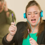 Une jeune femme en train d'écouter de la musique bruyamment à son bureau et un homme énervé en arrière-plan