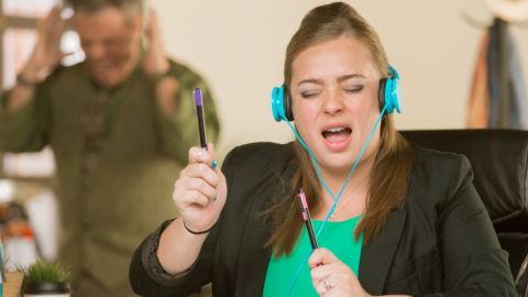 Une jeune femme en train d'écouter de la musique bruyamment à son bureau et un homme énervé en arrière-plan