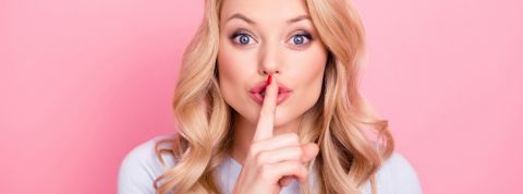 Les chiffres de l'infidélité féminine en 2019 Une femme blonde qui fait chut avec son doigt devant un fond rose