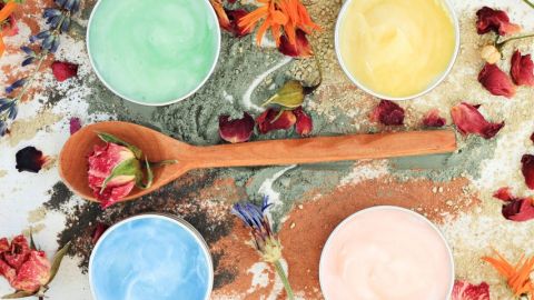 Plan de travail de cosmétique fait-main. Cuillère en bois avec une fleur, quatre pots de masques colorés faits-main autour