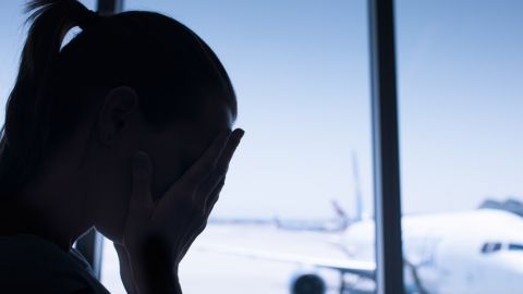 Silhouette d'une femme se cachant les yeux avec les mains, derrière elle un avion sur le tarmac.