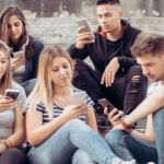 une bande de jeune assis sur des escalier qui regardent leur portables.