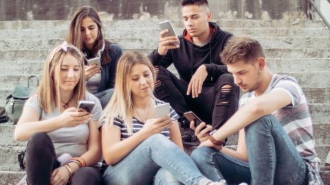 une bande de jeune assis sur des escalier qui regardent leur portables.
