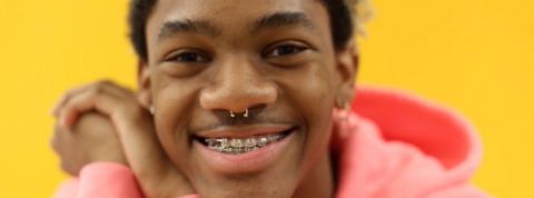 LGBTQ+ : comment les jeunes artistes réinventent la masculinité Un jeune porte portant des bagues aux dents et un sweat à capuche rose