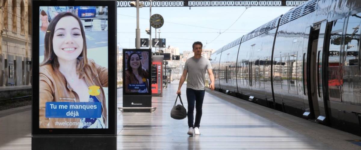Mediagare prolonge les aurevoirs Un homme regarde sa petite amie qui lui laisse un message sur les panneaux digitaux d'une gare