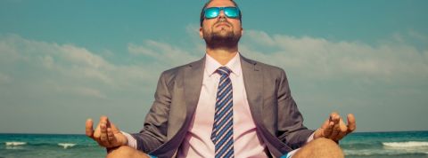 Les consultants se mettent au bien-être Un homme en costume en train de méditer sur la plage