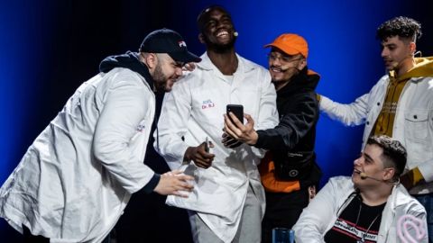 un groupe de jeunes homme en blouse blanche qui regarde un téléphone portable en rigolant