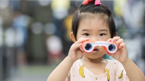 Une petite fille chinoise qui tient des jumelles dans les mains