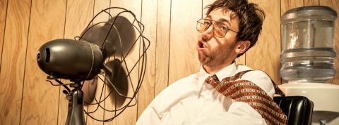 Comment faire face à la canicule au bureau ? Un employé de bureau en train de se rafraîchir avec un ventilateur