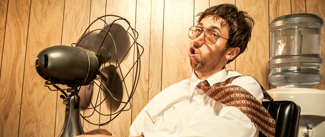 Comment faire face à la canicule au bureau ? Un employé de bureau en train de se rafraîchir avec un ventilateur