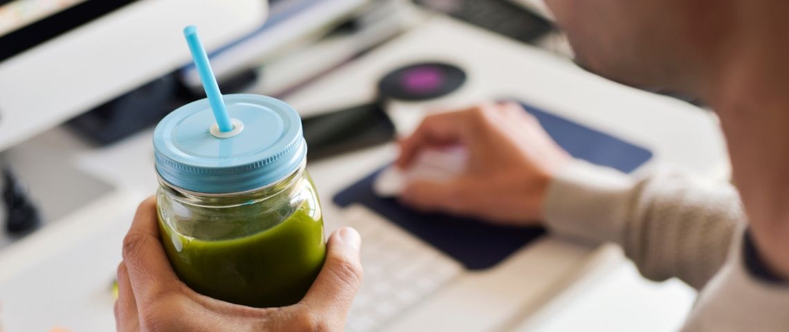 Comment être plus écolo au bureau ? Un employé de bureau boit un smoothie vert