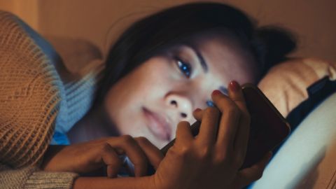 une jeune fille asiatique regarde un smartphone allongée dan un lit