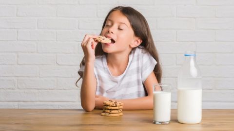 Un jeune enfant aux cheveux longs en train de manger un cookie trempé dans un verre de lait