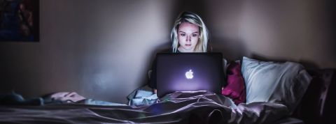 Ménage, sommeil, vie sociale : les 18-34 ans sacrifient tout pour leurs séries préférées Une jeune femme blonde regarde l'écran de son Macbook sur son lit