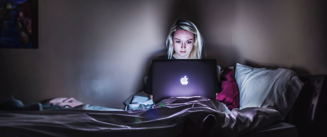 Ménage, sommeil, vie sociale : les 18-34 ans sacrifient tout pour leurs séries préférées Une jeune femme blonde regarde l'écran de son Macbook sur son lit
