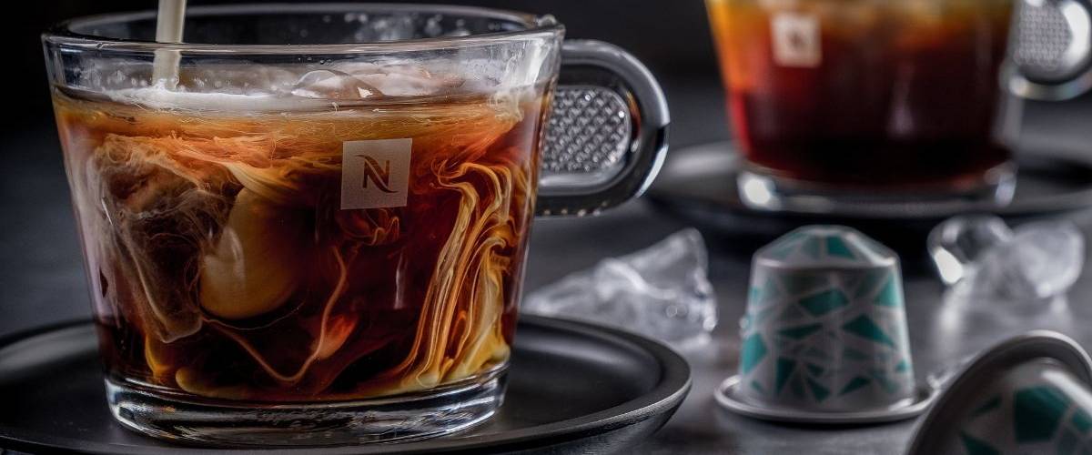 Nespresso déploie un système de recyclage pour ses capsules Sur une table se trouve une tasse de café Nespresso dans laquelle on verse un nuage de lait. A gauche, une capsule Nespresso