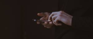 Deux mains tenant un smartphone, fond sombre.