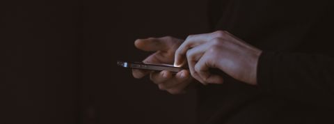 Des applis Android collectent vos données sans votre permission Deux mains tenant un smartphone, fond sombre.