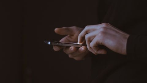 Deux mains tenant un smartphone, fond sombre.