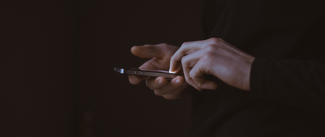 Des applis Android collectent vos données sans votre permission Deux mains tenant un smartphone, fond sombre.