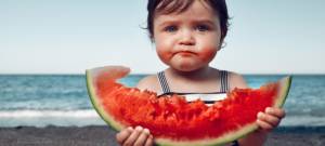 Une petite fille à la plage en train de manger une pastèque