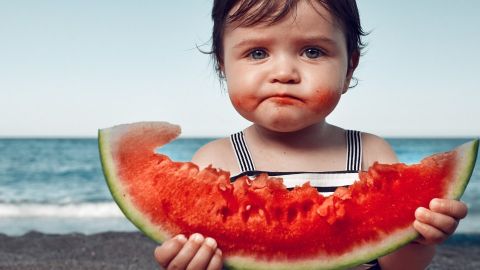 Une petite fille à la plage en train de manger une pastèque