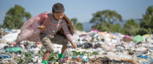 Un petit garçon en train de ramasser des déchets dans une décharge plastique à ciel ouvert