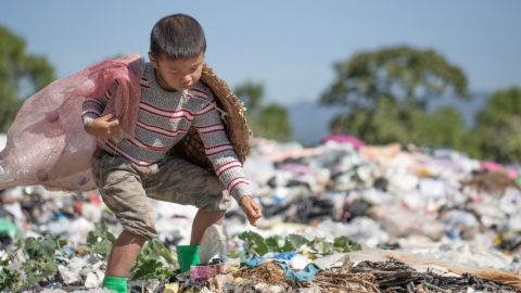 Un petit garçon en train de ramasser des déchets dans une décharge plastique à ciel ouvert