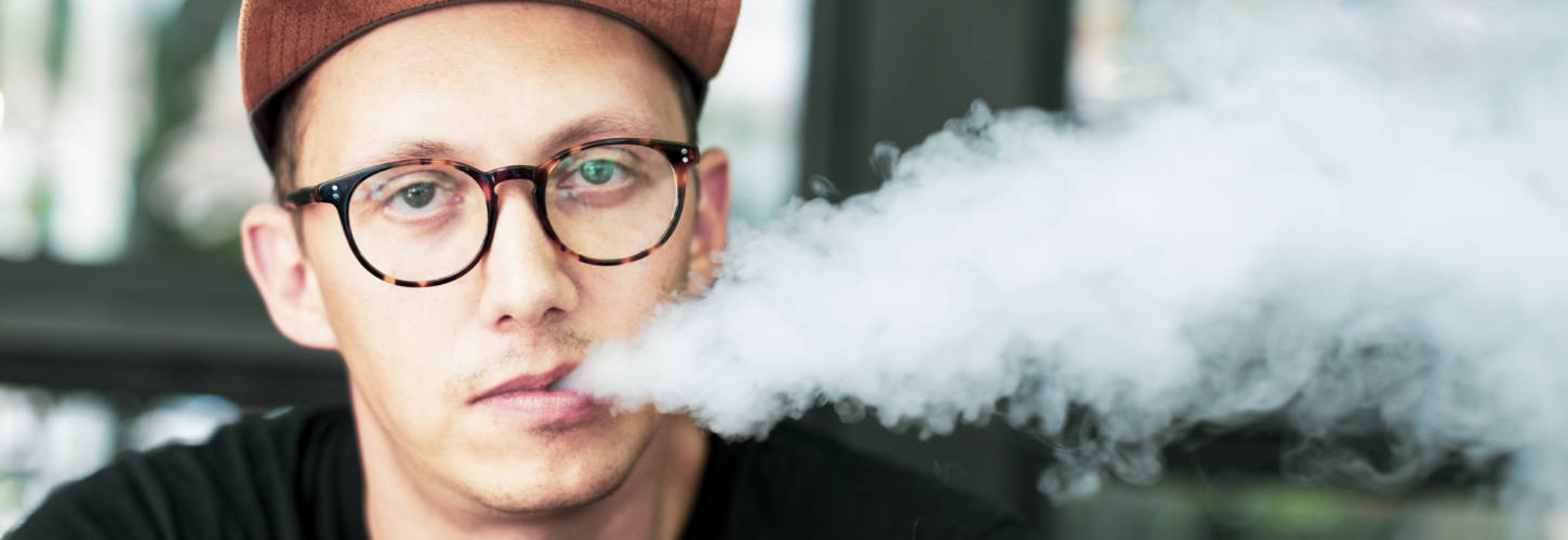 Caucasian man vaping at an outdoor cafe jeune homme fumant une ecigarette en faisant de la fumée