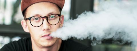 Caucasian man vaping at an outdoor cafe jeune homme fumant une ecigarette en faisant de la fumée