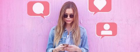 Quels influenceurs choisir pour optimiser sa campagne en ligne ? Une jeune femme en veste en jean posant devant un fond rose et utilisant son téléphone portable